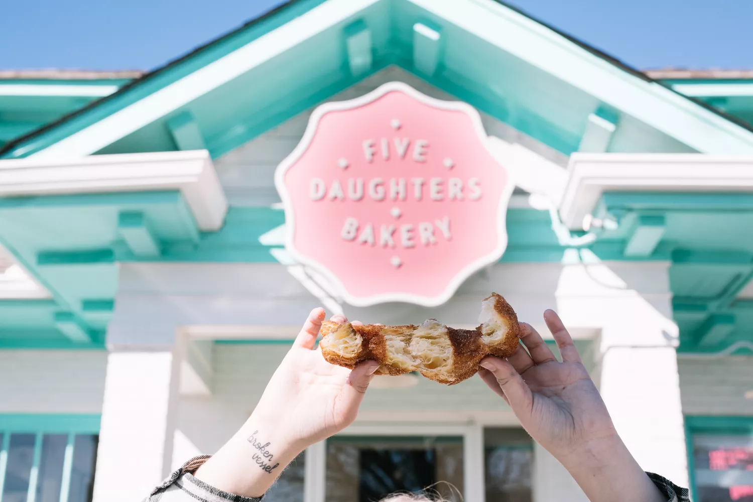 Hands pulling apart a pastry in front of Five Daughters Bakery