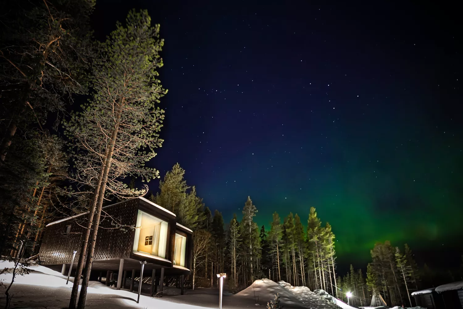 A glass cabin lit at night looking out at northern lights