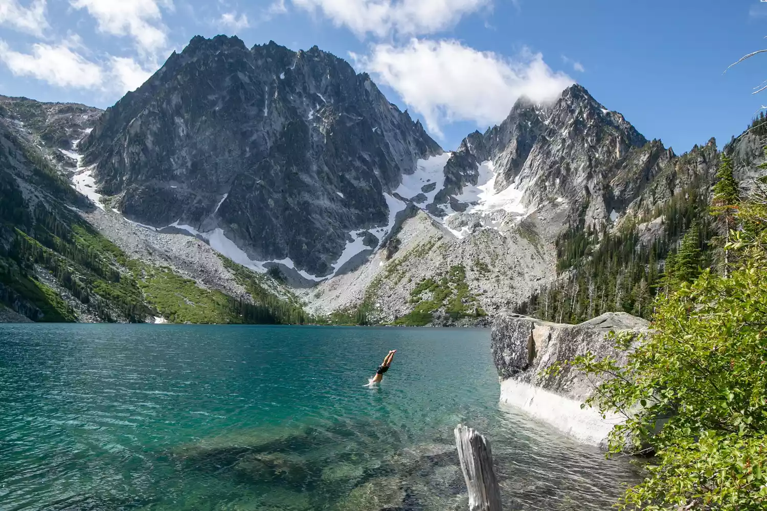 A person diving into Colchuck lake surrounded by mountains