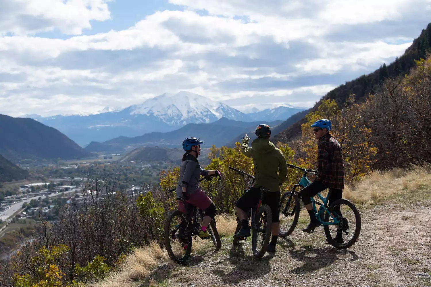 Trois personnes à VTT s'arrêtent pour admirer la vue sur les montagnes enneigées depuis un sentier à Glenwood Springs, CO