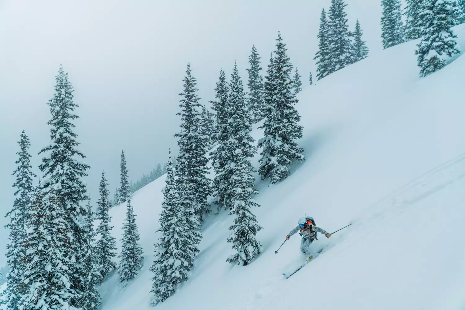 A skiier going down a mountain by snow covered trees