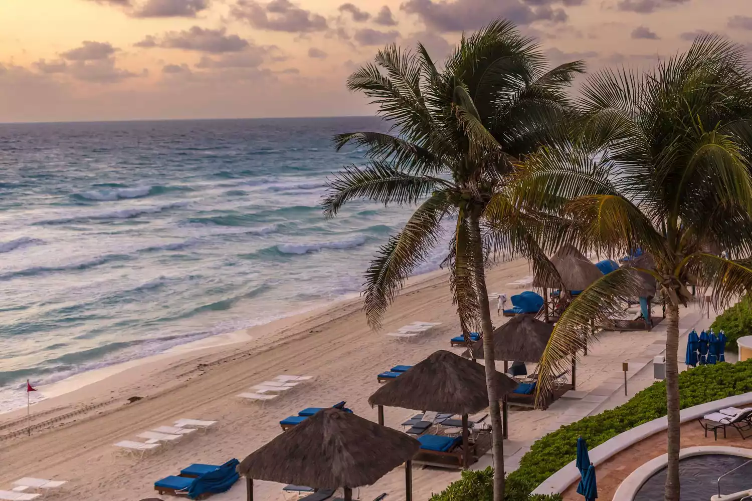 View from suite's terrace of the beach with palm trees and cabanas below and beautiful early sunset 