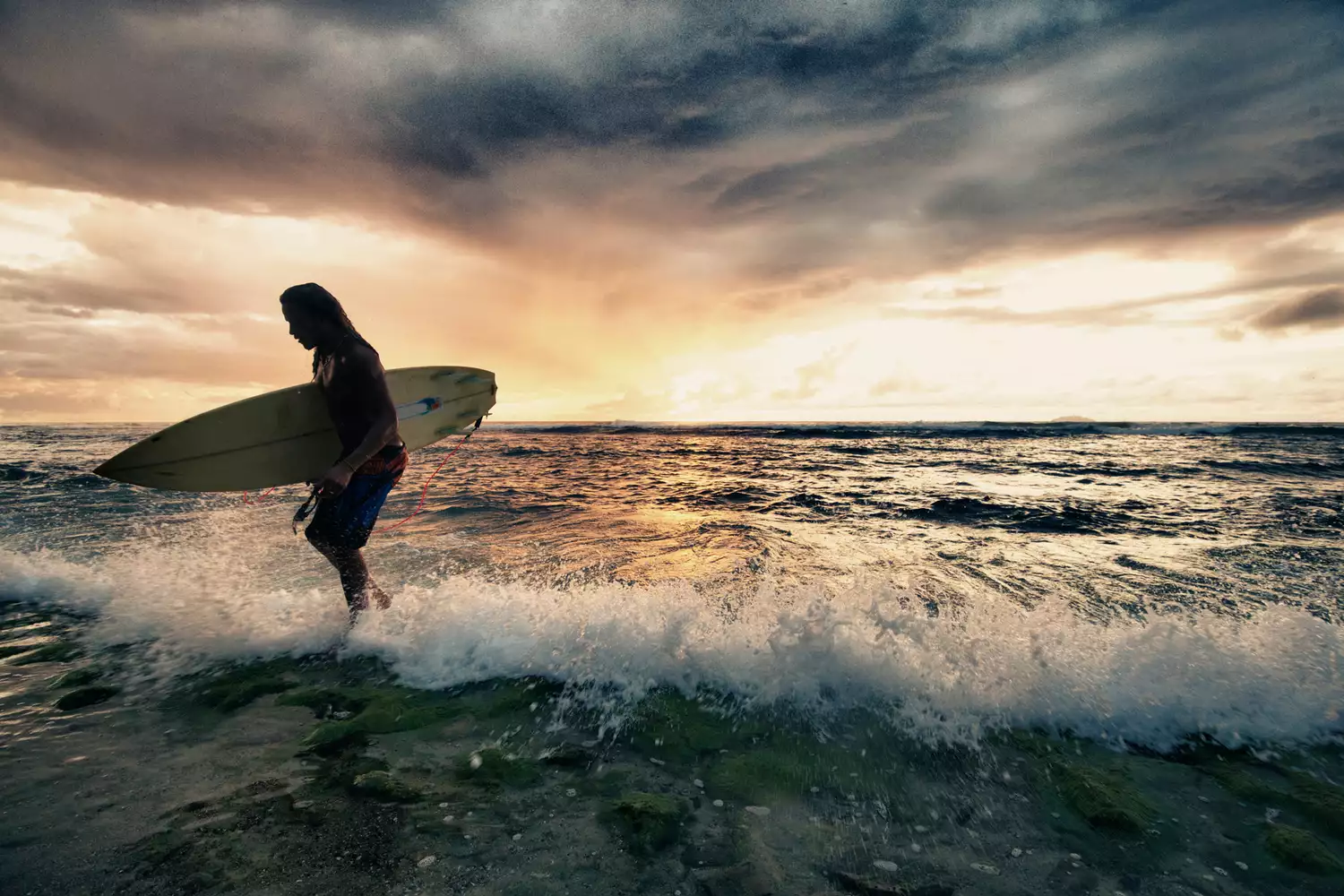 Surfeur sortant de l'eau avec sa planche de surf au coucher du soleil à Rincón, Puerto Rico