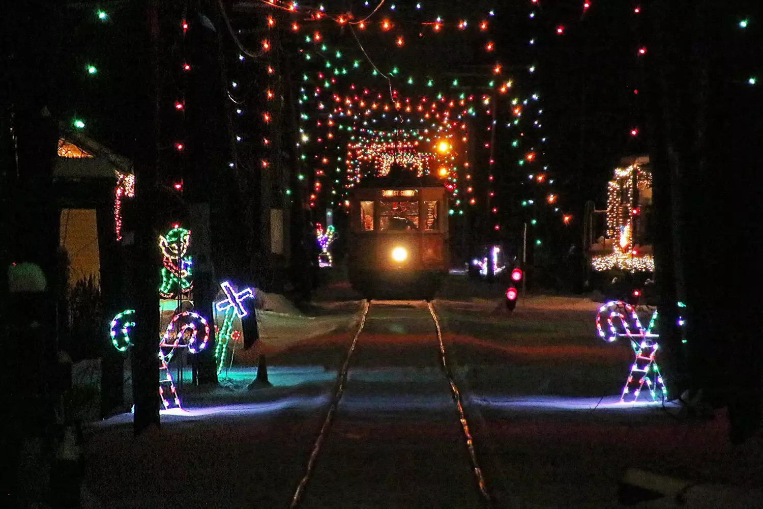 a trolley coming down a track at night surrounded by christmas lights