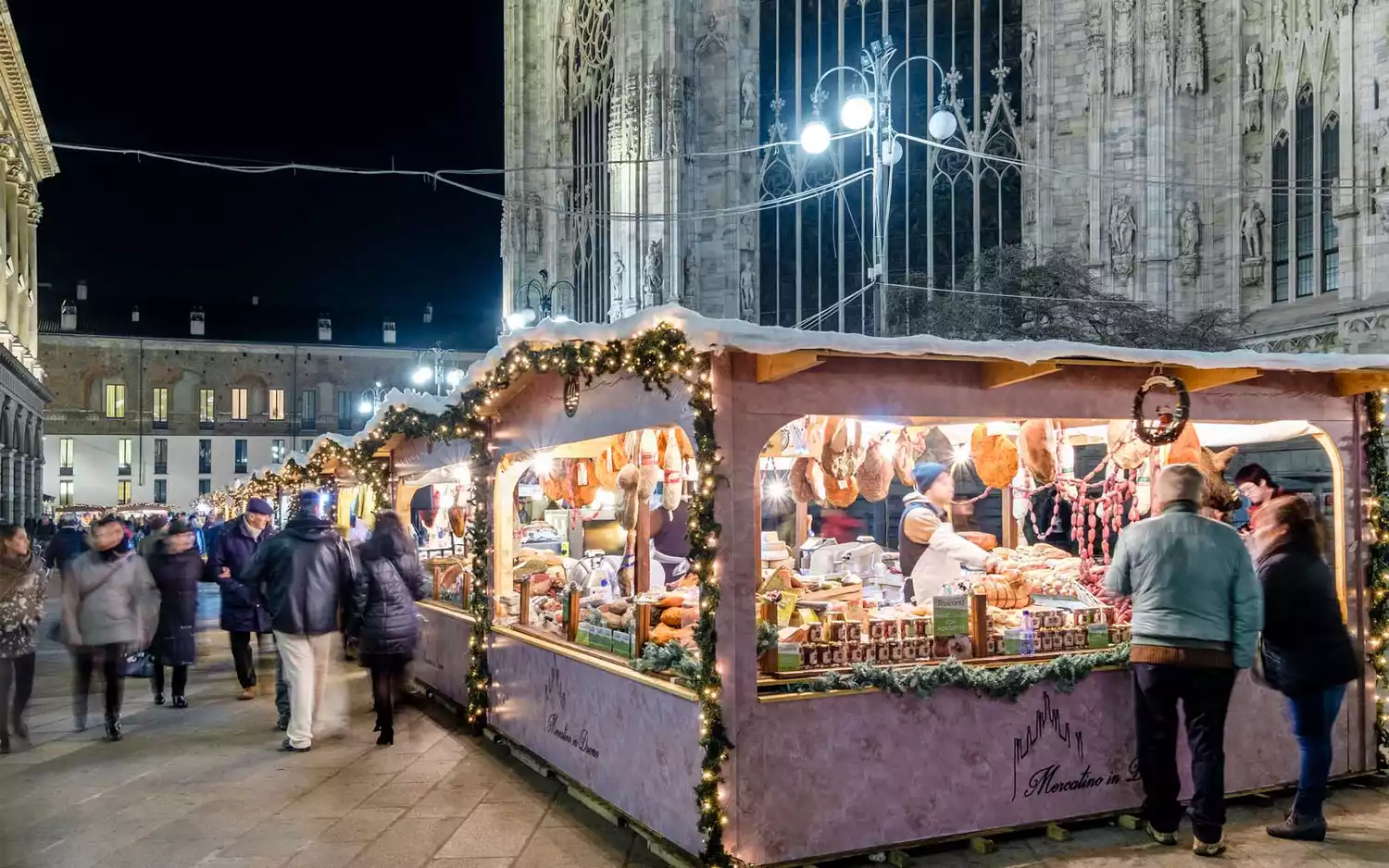 Visitors shop for meat at a Christmas market stall in front of Milan's Duomo cathedral.