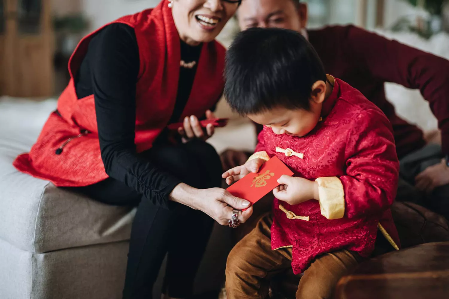 Un petit-fils vêtu d'un costume traditionnel chinois rouge reçoit joyeusement des enveloppes rouges (lai see) de ses grands-parents pour le Nouvel An chinois.