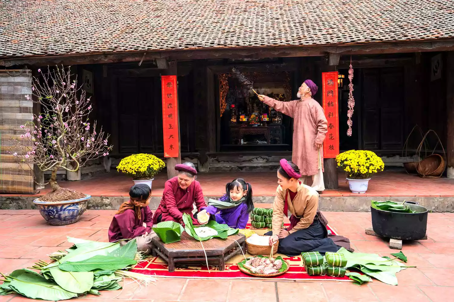 Membres de la famille vietnamienne préparant ensemble le Banh Chung dans une cour de maison de style ancien. Le gâteau Chung est un plat très connu qui ne peut jamais manquer sur l'autel et le repas familial des Vietnamiens pendant les vacances de Tet