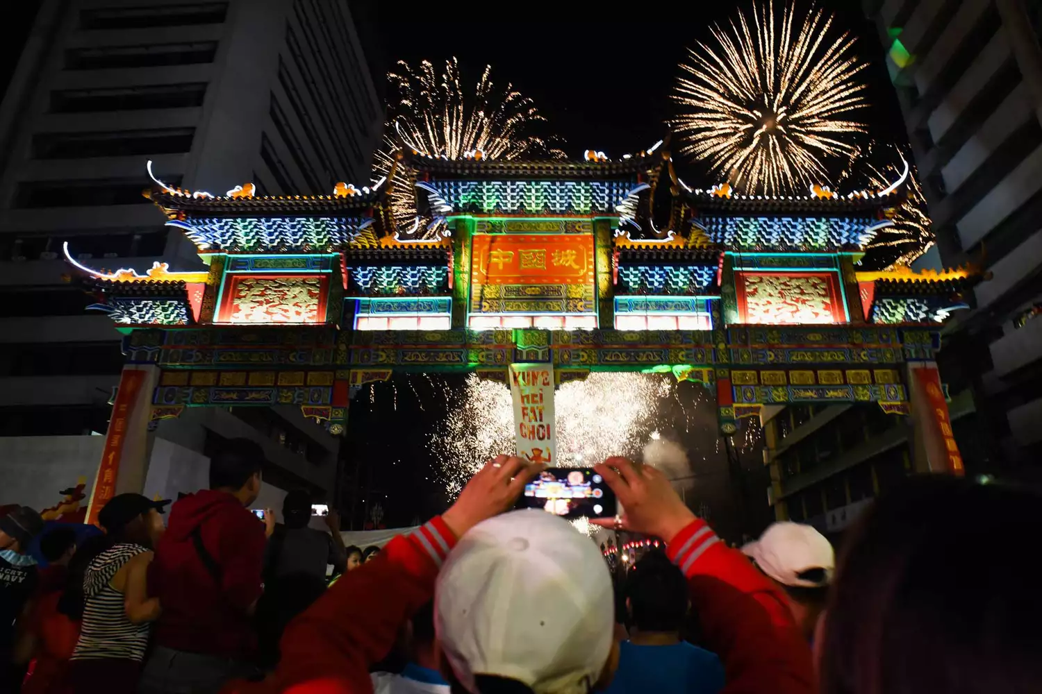 Un homme filme la scène avec son téléphone portable alors que des feux d'artifice illuminent le ciel au-dessus de l'arche de l'amitié de Chinatown, la plus grande au monde, située dans le quartier de Binondo, le Chinatown de Manille, à la veille du Nouvel An chinois, à Manille, aux Philippines