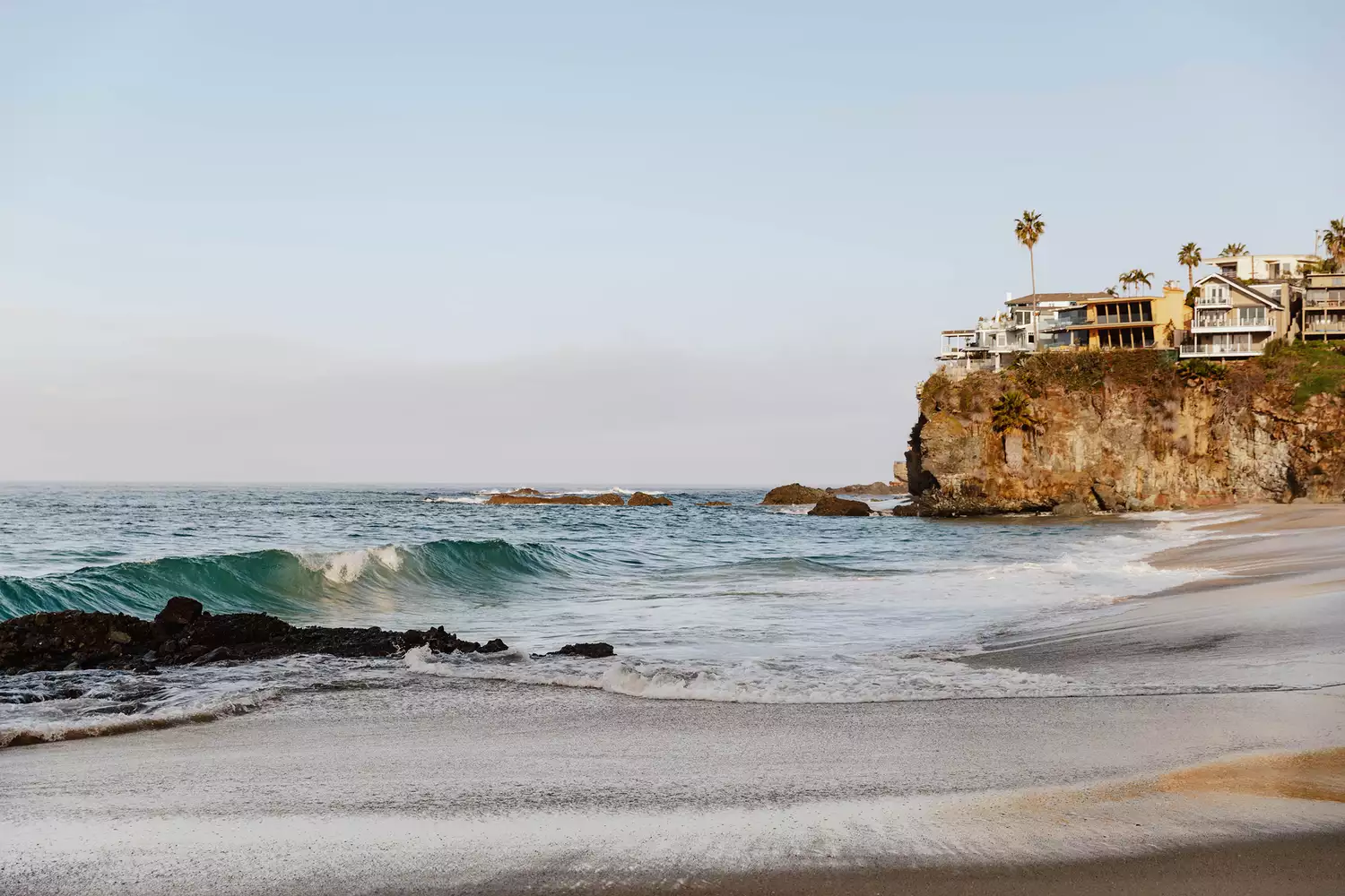 Vagues se brisant sur une plage avec des maisons sur une falaise au loin - Thousand Step Beach à Laguna Beach, CA